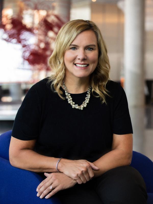 Amy Davis wearing all black with a statement necklace, sitting in a blue chair