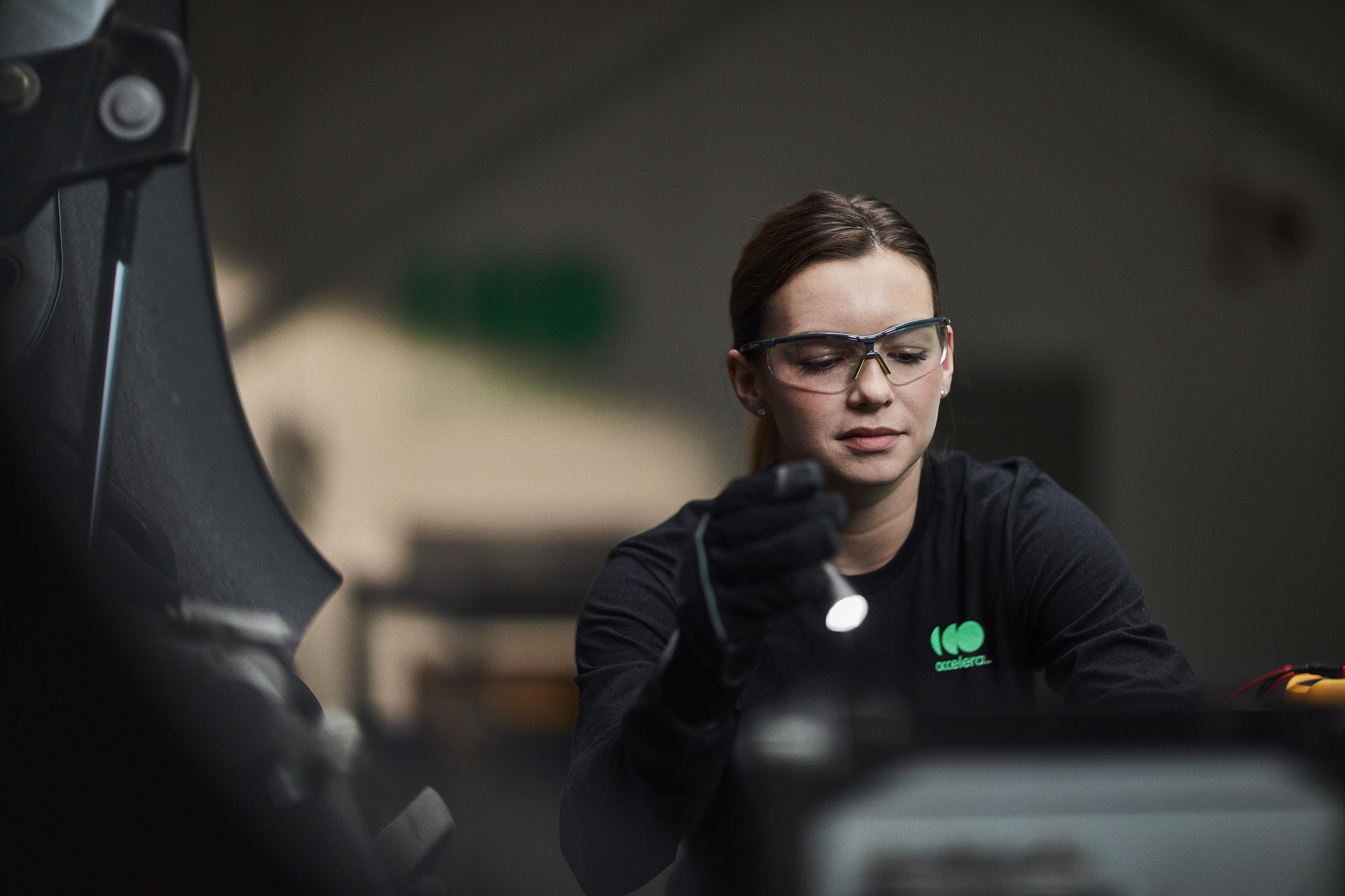 Female engineer wearing safety glasses while working under the hood of an Accelera-powered zero-emissions vehicle